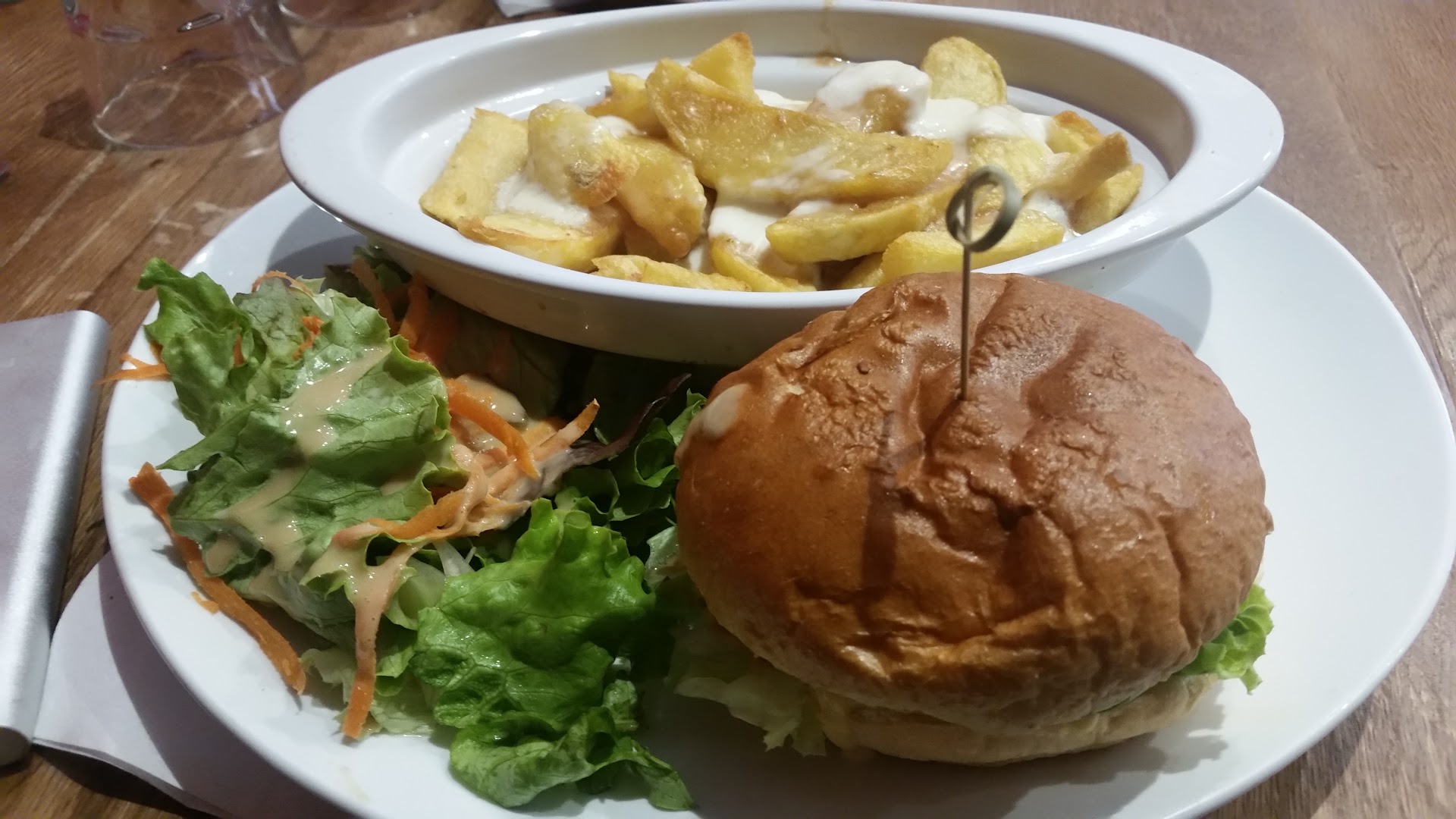 Un burger servi avec des frites en sauce et une salade